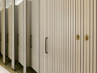 Large resort bathroom features six full size, grey compact laminate partitions and doors with vertical engraving that displays black lines.