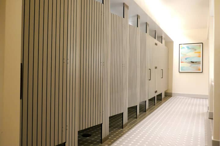 Large resort bathroom features six full size, grey compact laminate partitions and doors with vertical engraving that displays black lines.