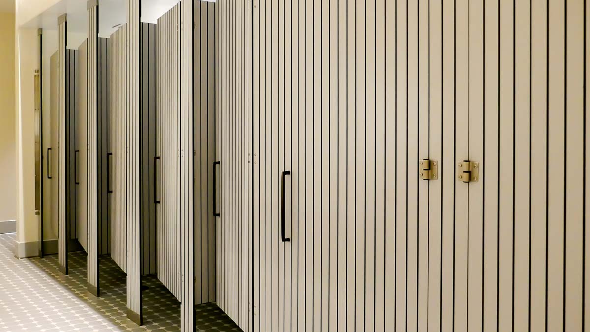 Large resort bathroom features six full size, grey compact laminate partitions and doors with vertical engraving that displays black lines.