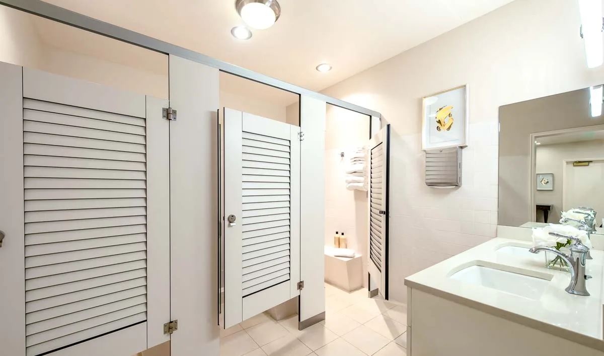 Country Club locker room with pretty white compact laminate louver doors opposite vanity and mirror. Open door shows changing area leading to shower.