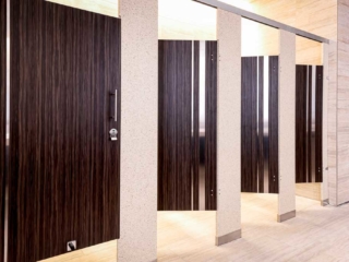 Majestic casino bathroom with solid surface pilasters and four plastic laminate wood grain opened doors with vertical stainless steel insert strips.