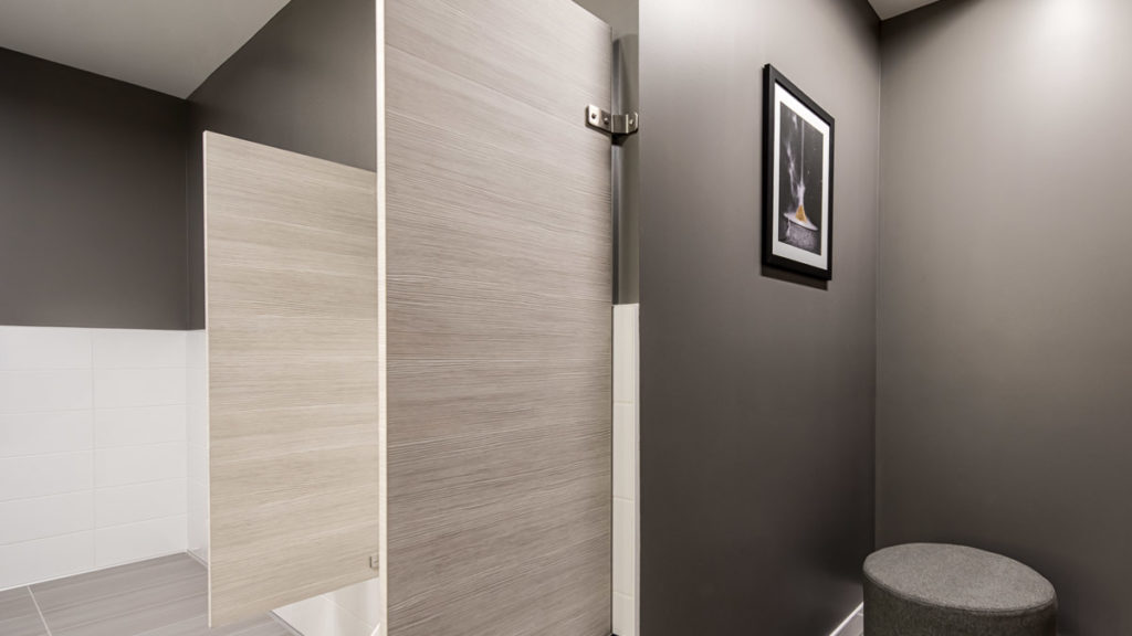 Dark grey walled men’s bathroom including laminate privacy screens between urinals made with Laminart in textured grey hues.