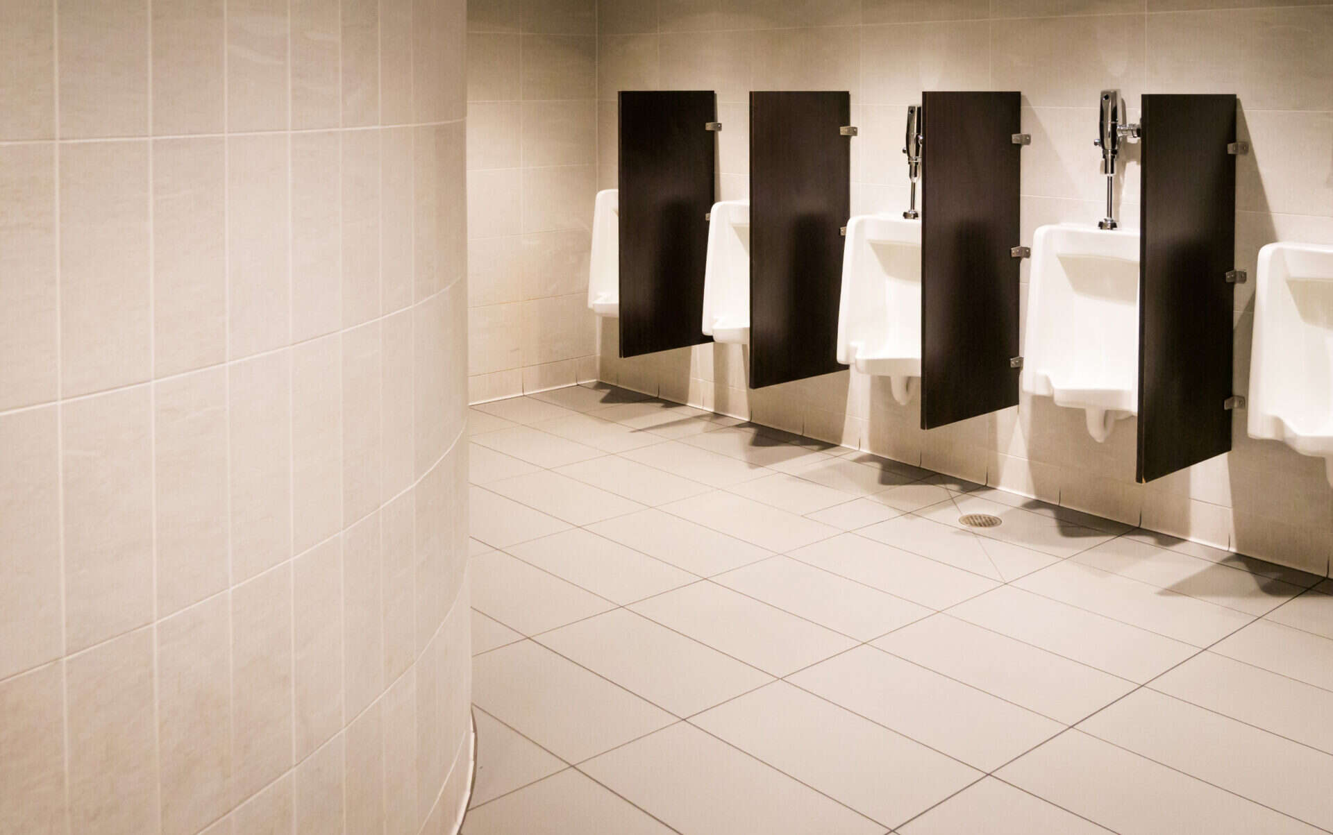 Dark grey walled men’s bathroom including laminate privacy screens between urinals made with Laminart in textured grey hues.