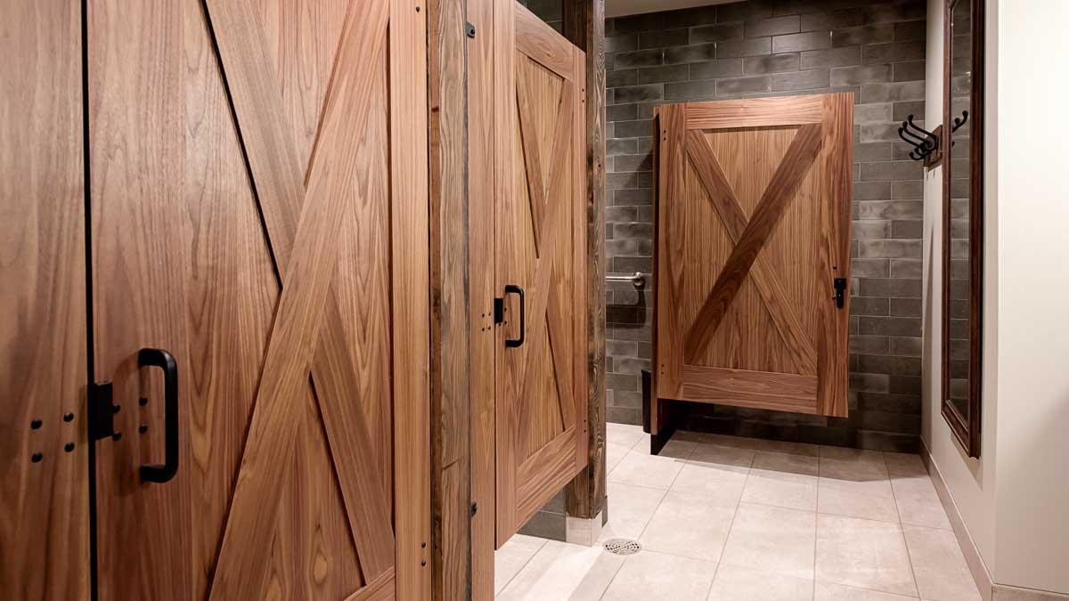 Luxury Montana lodge bathroom displaying three wood veneer captured panel doors with large X shape on both sides of doors in dark subway tiled room.