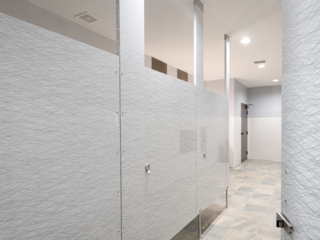 Modern university clubhouse bathroom features four slab doors in gloss plastic laminate featuring wavy grey patterned lines on white background.