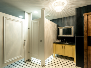 Designer showroom bathroom with white laminate partitions show doors with picture frame molding. Yellow vanity, silver framed mirror and chandelier.