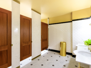 Swanky business headquarters tiled bathroom features engineered stone pilasters with three wood veneer, captured panel doors with bronzed hardware.