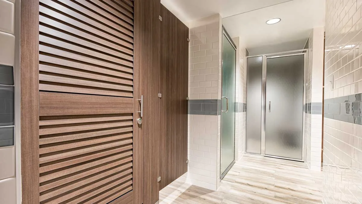 White tiled spa bathroom featuring green glass door shower and private dressing compartment with traditional brown louver doors.