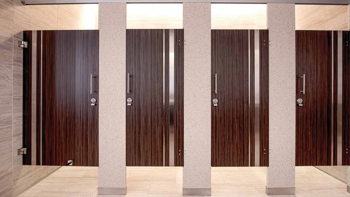 Glamorous casino bathroom with solid surface pilasters and four plastic laminate dark, wood grain doors with vertical stainless steel insert strips.