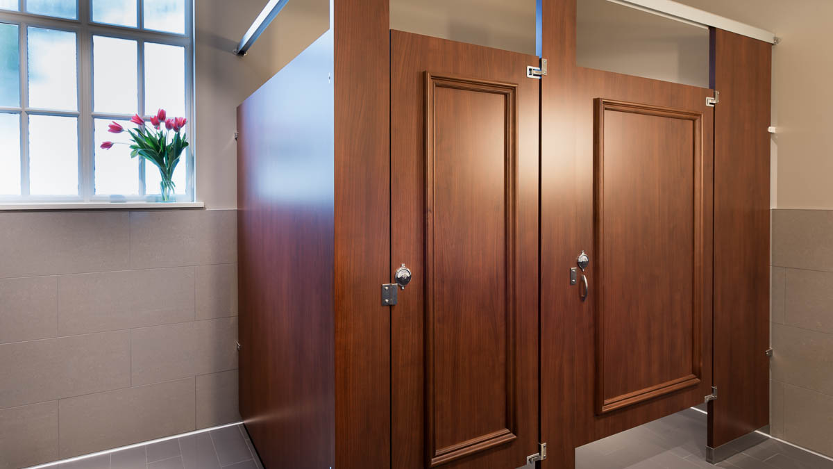 Beautiful full height, wood grain plastic laminate partitions with two doors featuring picture frame molding. Tulips on window seal in club bathroom.