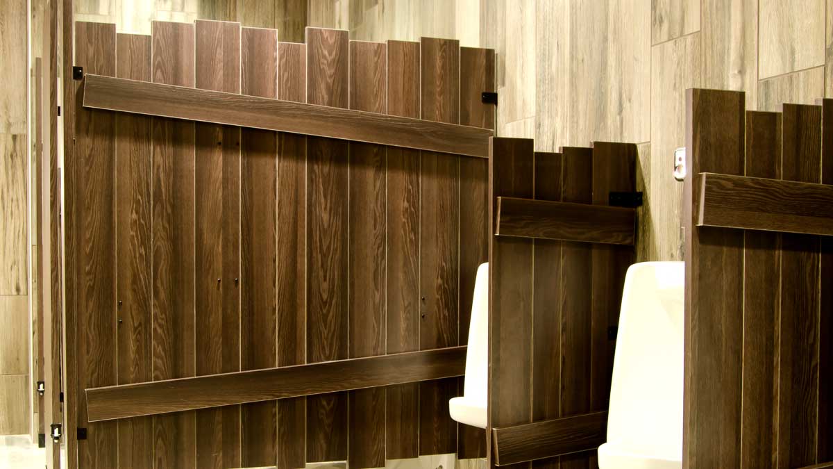 Custom shape laminate bathroom partitions with purposeful uneven edges on brown, outhouse look compartment and privacy screen between urinals.
