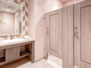 Country Club bathroom featuring compact laminate partitions with light tan, wood grain captured panel doors. Elegant vanity with chevron wallpaper.