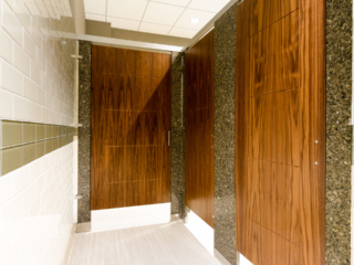 White subway tiled business showroom bathroom featuring three rich wood grain, engraved veneer doors with grey speckled engineered stone pilasters.