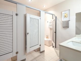 Three, pretty white compact laminate louver dressing compartments opposite vanity and mirror. Open door shows changing area with bench and towels.