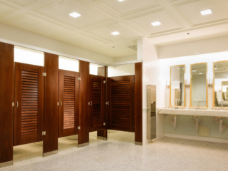 Elegant reception venue bathroom with coffered ceiling showing wood veneer pilasters and five louver doors with three gold rimmed mirrors over vanity.