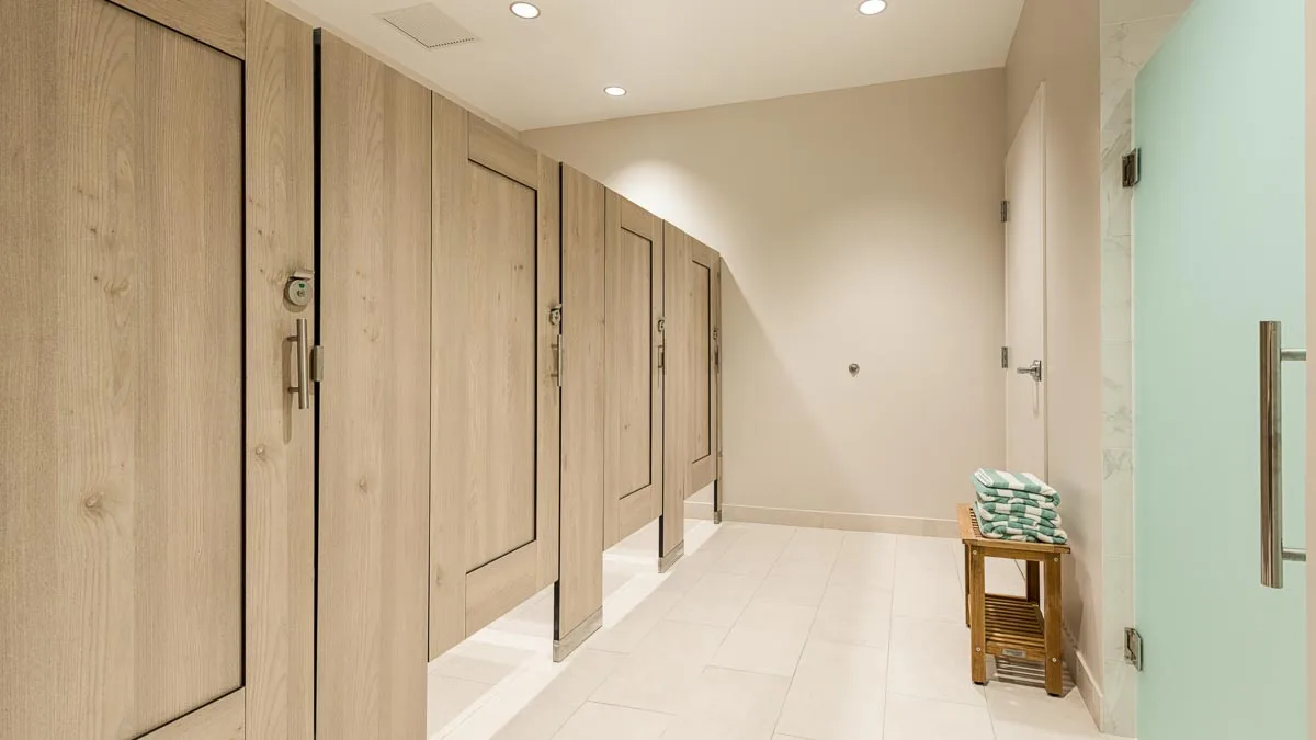 Country Club bathroom shows compact laminate dressing compartments with light tan, wood grain captured panel doors opposite frosted green shower door.