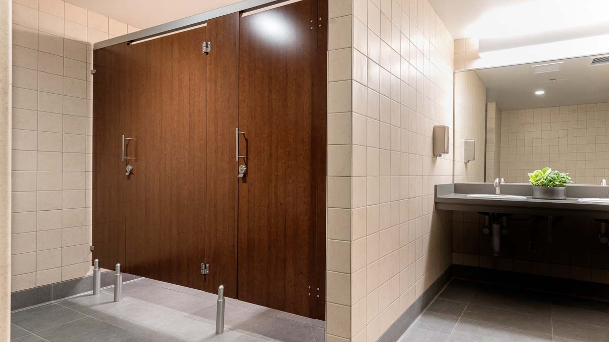 Two door glossy brown, plastic laminate oversize european style bathroom partition has a clean, modern appearance in government building.
