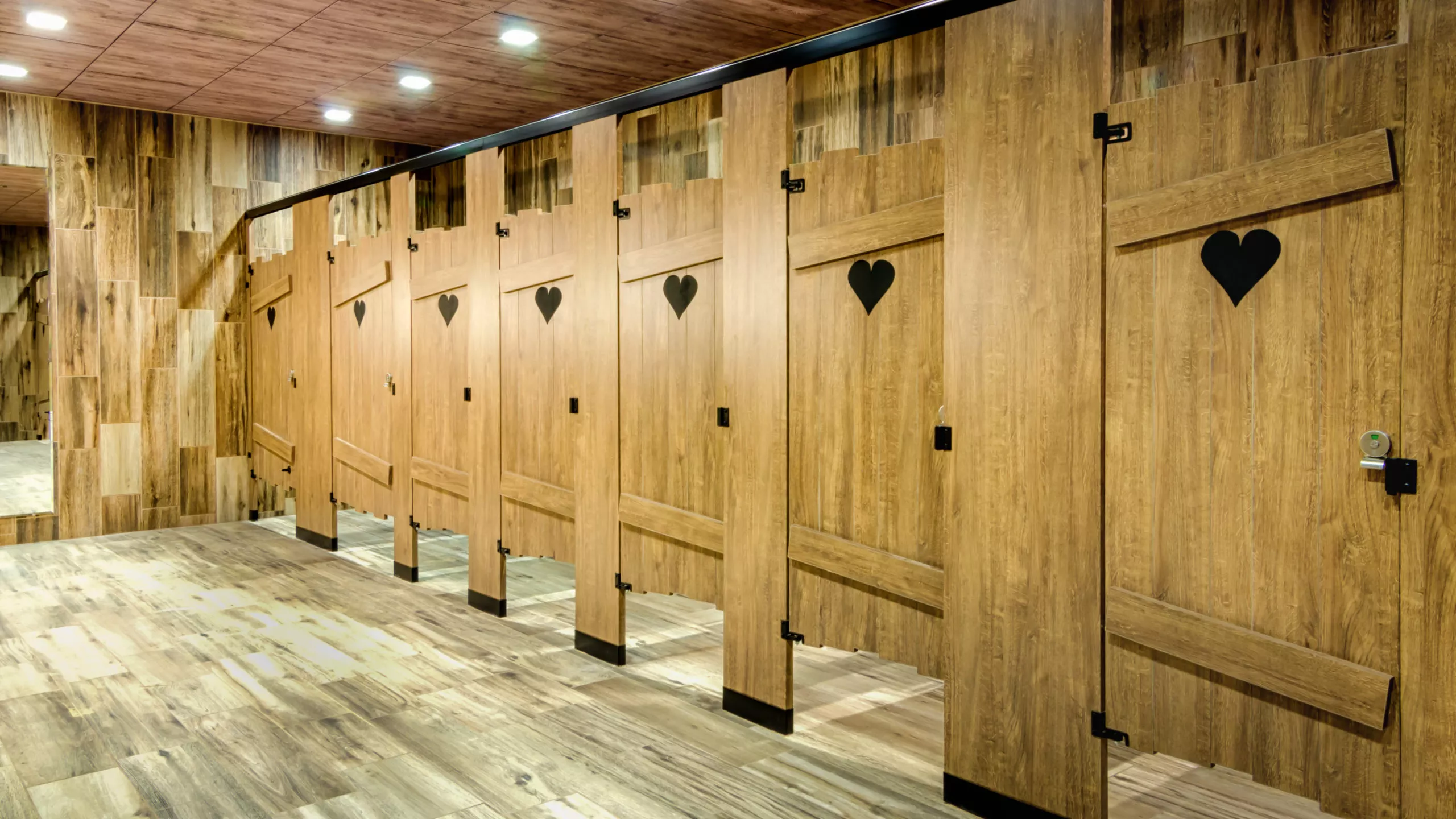 Custom commercial restroom partitions constructed like outhouses with powder coated hardware and engravings.