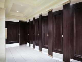 Seven full height dark wood grain laminate bathroom partitions and doors accented with picture frame molding stained to match laminate.