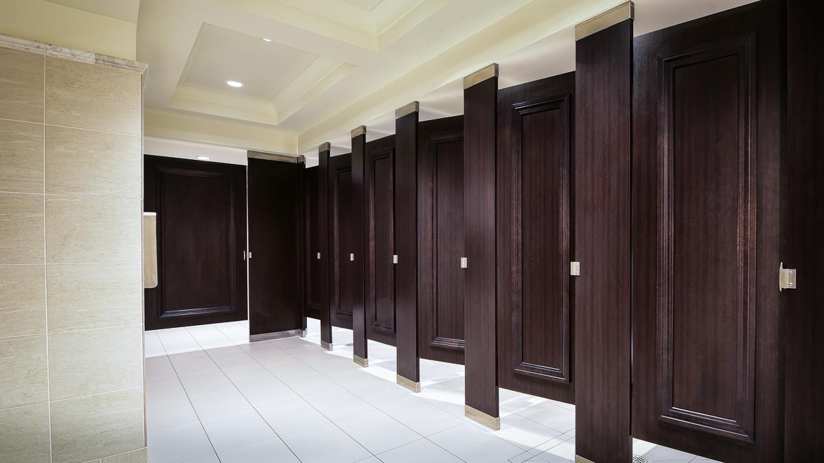 Seven full height dark wood grain laminate bathroom partitions and doors accented with picture frame molding stained to match laminate.