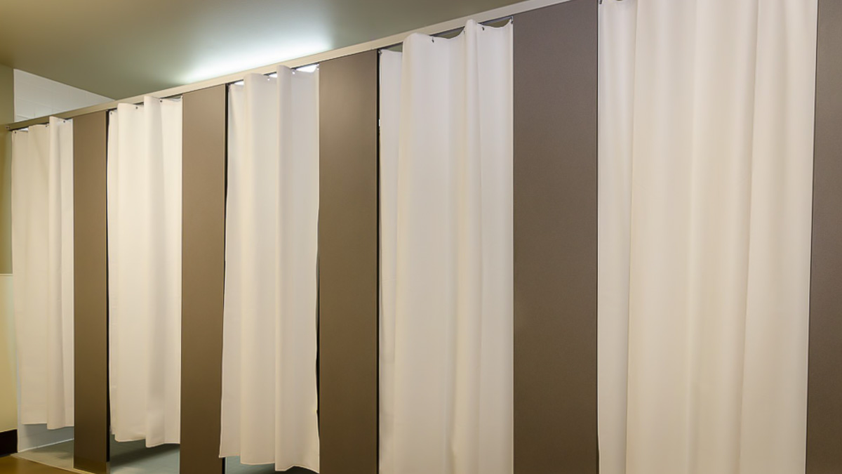 Five shower partitions with closed white curtains. The pilasters are made from compact laminate in a headrail braced configuration.