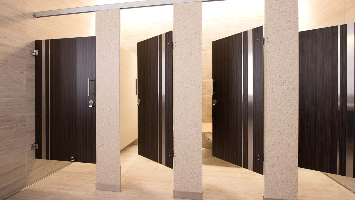 Chic casino bathroom with solid surface pilasters and four plastic laminate wood grain opened doors with vertical stainless steel insert strips.
