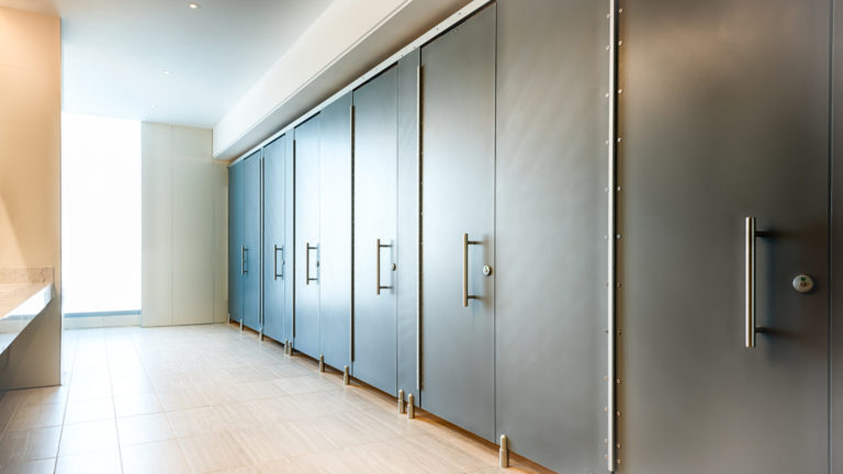 Solid surface high-privacy European bathroom stalls with headrail bracing, pedestals, and full length door pools in a commercial restroom.