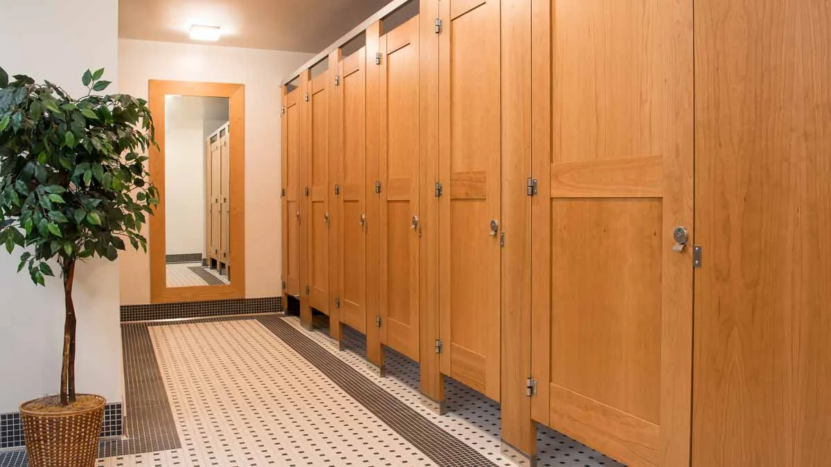 Black and white tiled theater bathroom with six full height wood veneer partitions featuring captured panel doors with mid rail.
