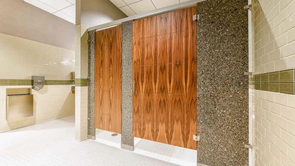 White subway tiled bathroom shows two rich wood grain, engraved veneer doors with grey speckled engineered stone pilasters in headrail braced style.