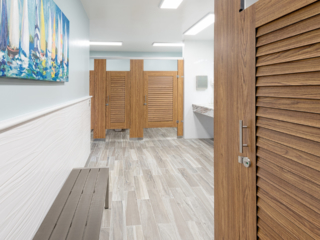 Marina bathroom features compact laminate, wood grain louver doors in headrail braced style. Sailboat print on wall above grey metal changing bench.