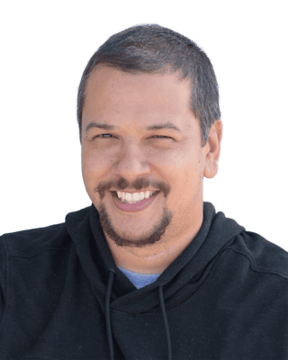 A person with short hair and facial hair smiles while wearing a black hoodie.