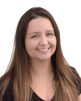 Woman with long brown hair smiling, wearing a black shirt and a necklace, on a plain background.