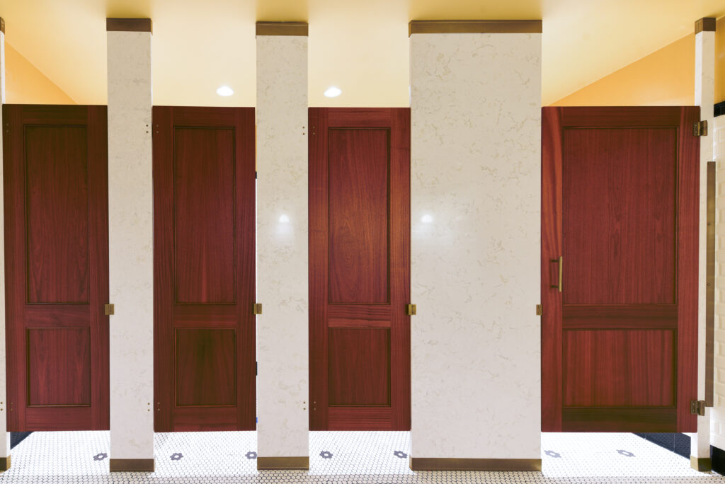 Floor to ceiling wood veneer toilet stalls in a bathroom.