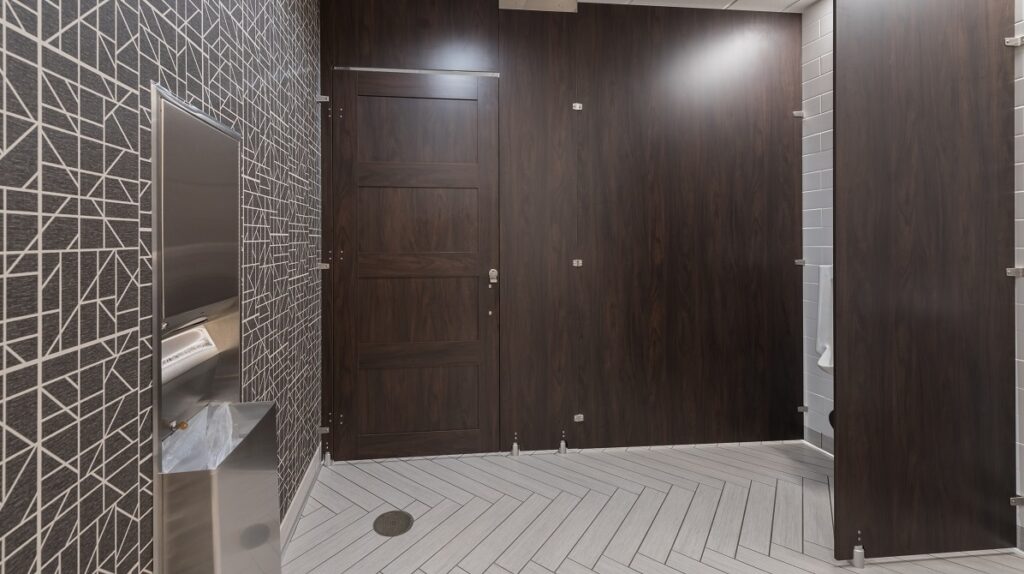 A bathroom with a sink and floor to ceiling toilet partitions.