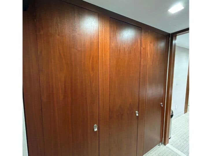Wooden closet doors with silver handles stand gracefully in the hallway, illuminated by a ceiling light. The carpeted floor complements the warm tones, while a T Bracket discreetly supports the structure for added stability and elegance.