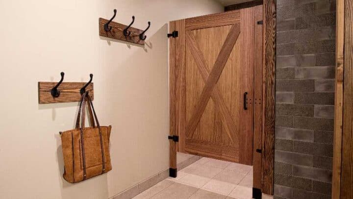 A wooden door with black hinges is next to a tiled wall; two wooden coat racks with hooks are mounted on the wall, one holding a brown leather bag.