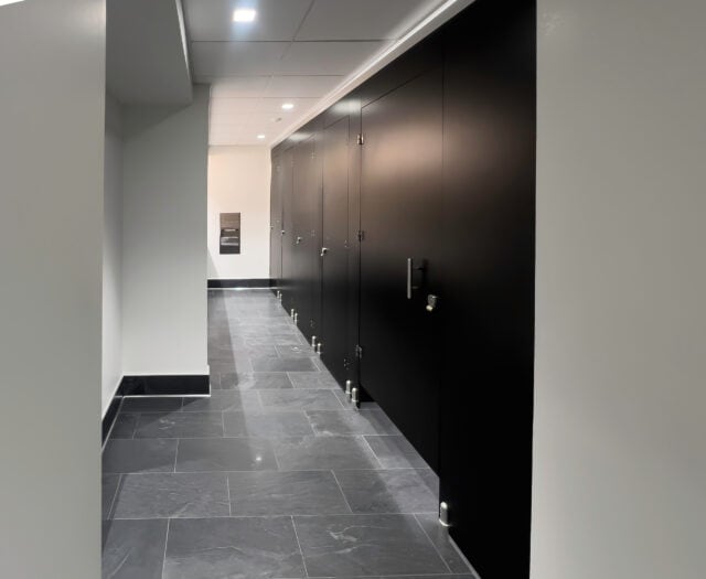 Public restroom with black stall doors, gray floor tiles, and a silver paper towel dispenser on the wall.