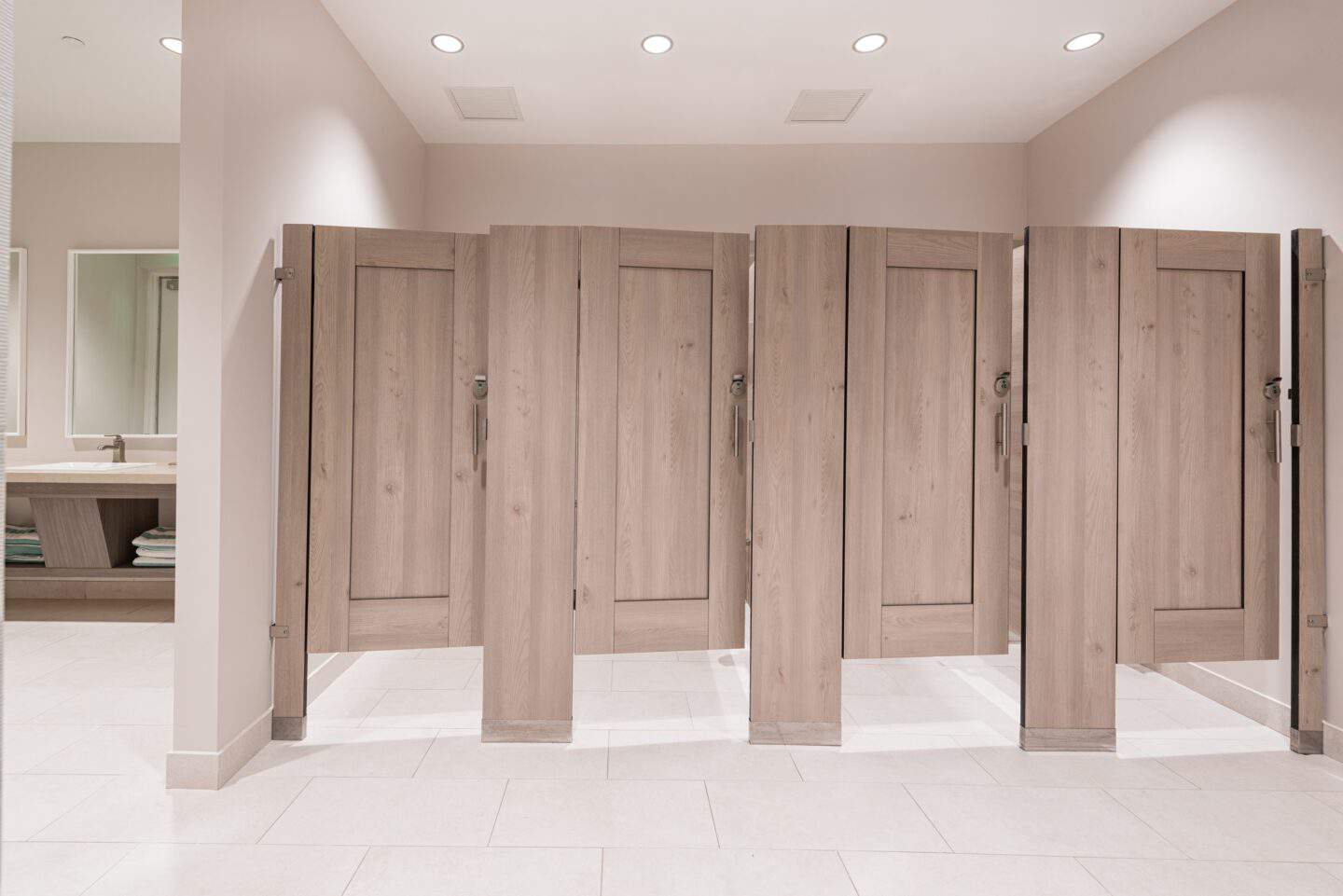Four captured panel floor mount commercial restroom partitions in woodgrain compact laminate with indicator latches and pulls.
