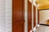 A row of wooden restroom stall doors with white tiled walls and floor in a well-lit bathroom.