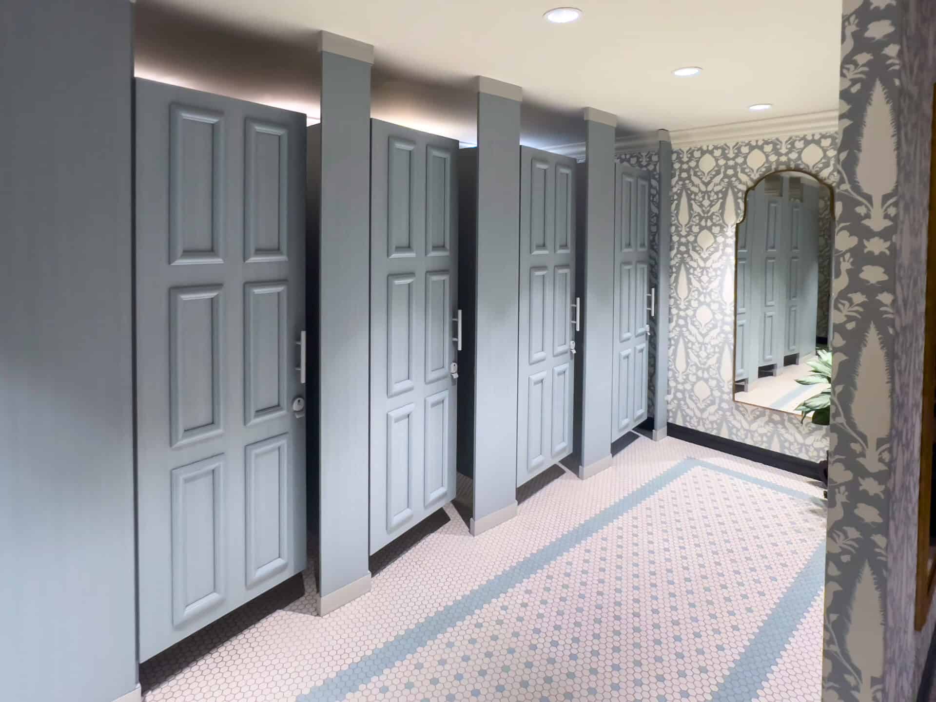 A row of light blue restroom stalls with zero sightline commercial restroom partitions and closed doors, plus a large wall mirror in a brightly lit, patterned bathroom—an ideal privacy solution.