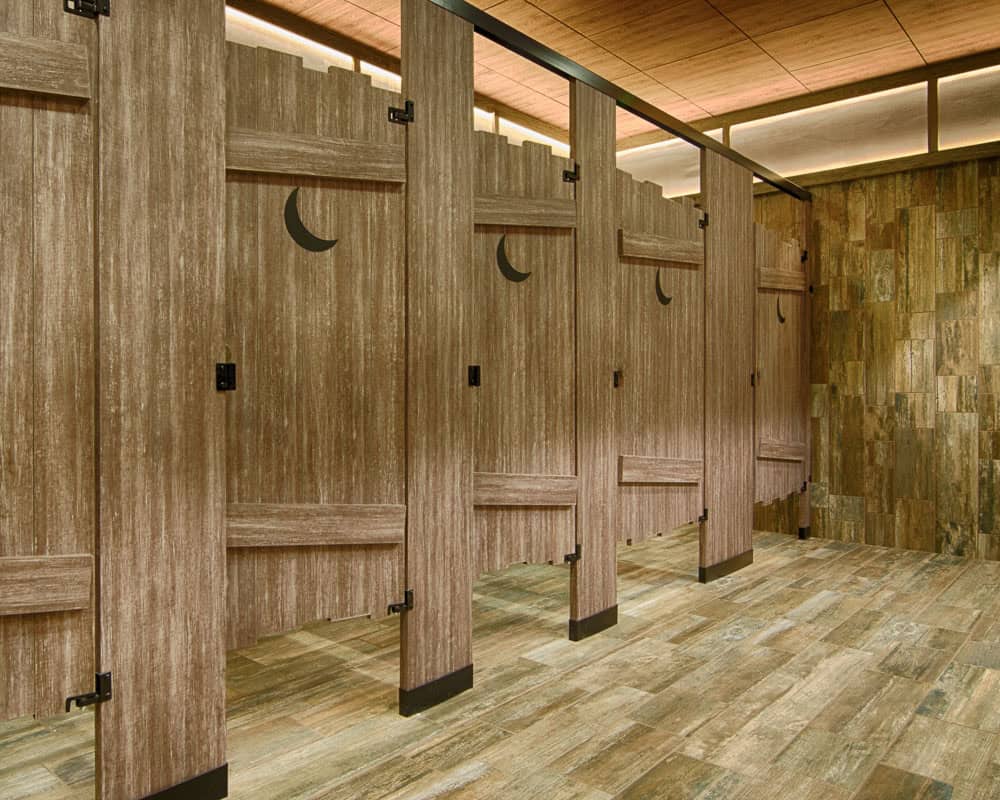 Three restroom stalls with wooden barn-style doors featuring crescent moon cutouts.