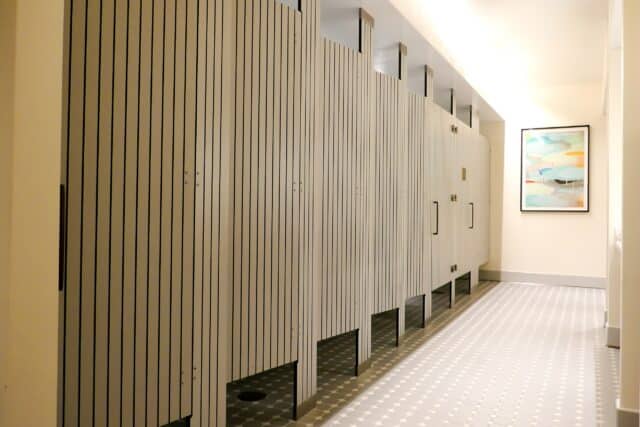 A row of compact laminate floor to ceiling mounted toilet partitions with engravings, a tiled floor, and a picture on the wall.