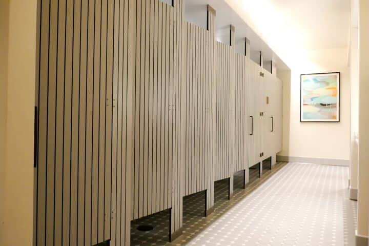 A row of compact laminate floor to ceiling mounted toilet partitions with engravings, a tiled floor, and a picture on the wall.