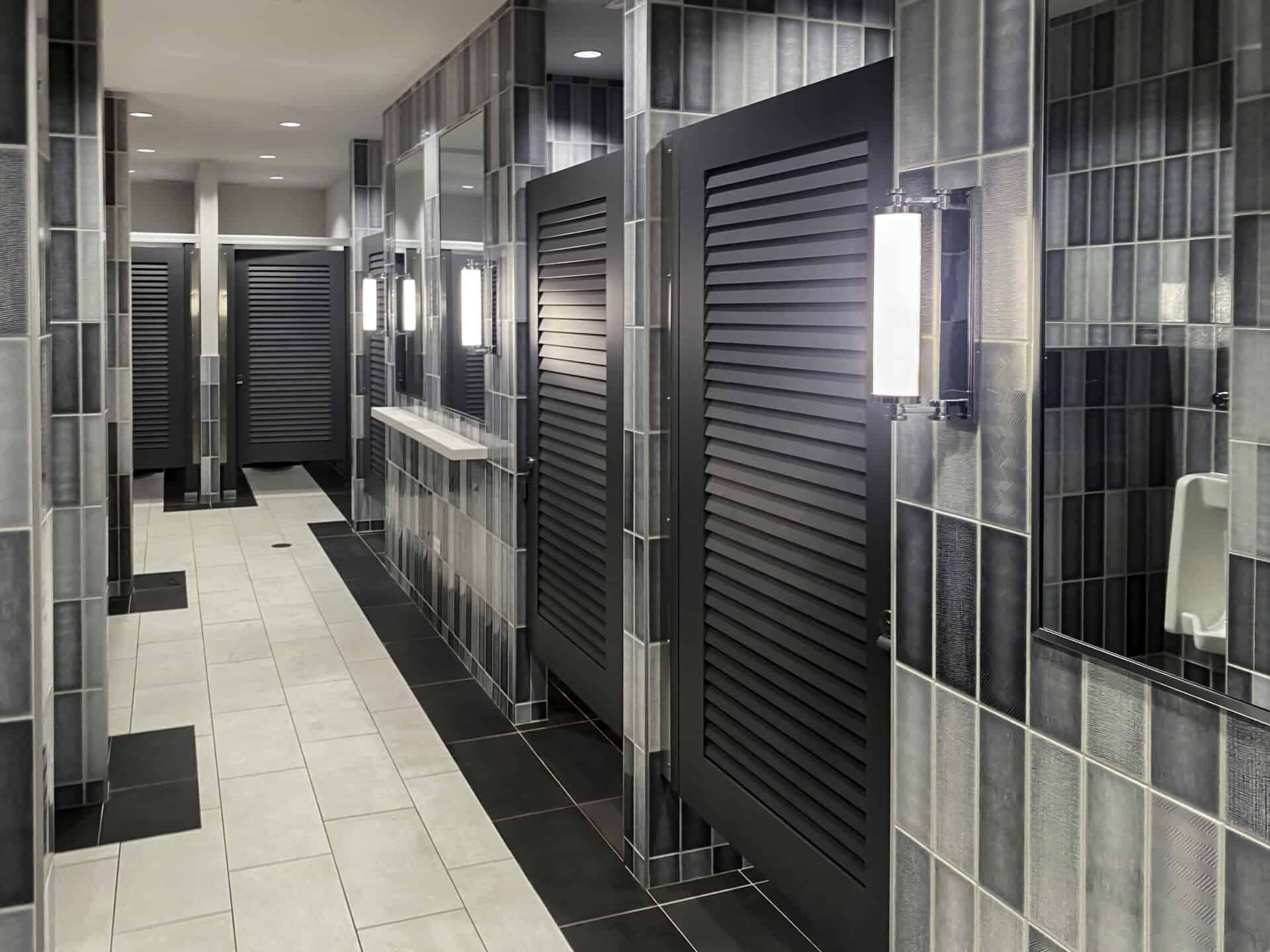 Black louvered bathroom partition doors in a headrail-braced system.