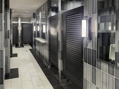 Black louvered bathroom partition doors in a headrail-braced system.
