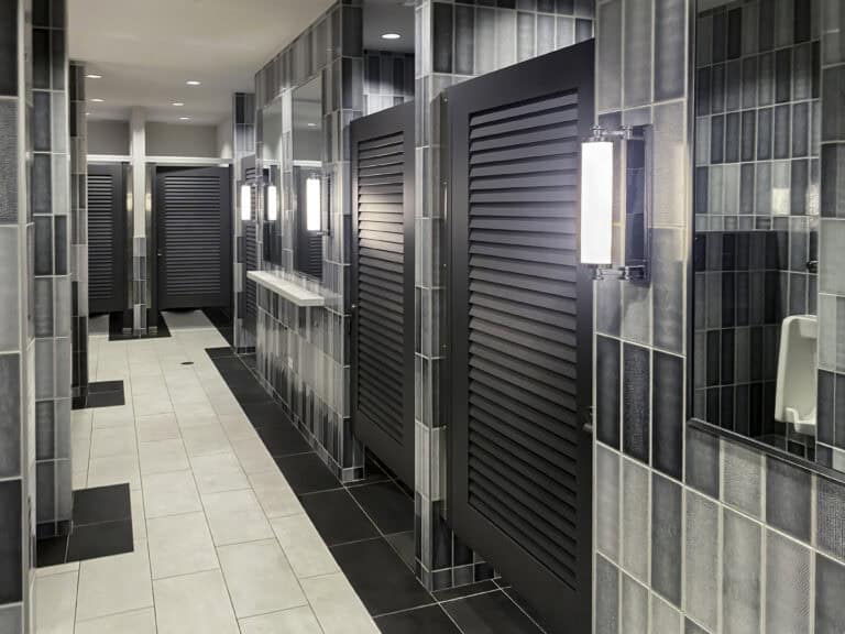 Black louvered bathroom partition doors in a headrail-braced system.