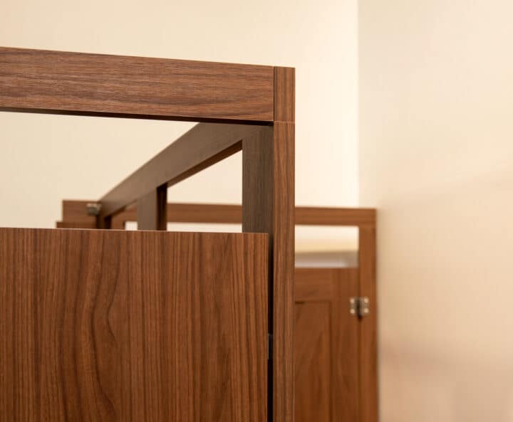 Wooden restroom partitions with custom headrail matching the door with a modern design in a corner of a light-colored restroom.