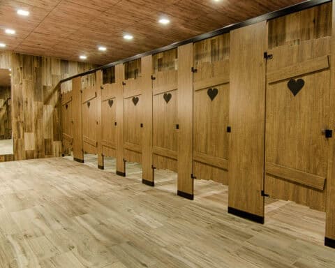 Custom shape commercial restrooms built like outhouse stalls with an engraved heart and slats on the doors.