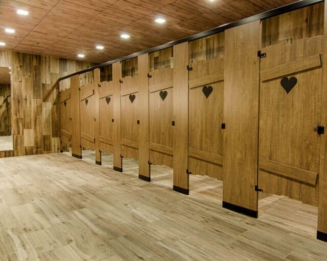 Custom shape commercial restrooms built like outhouse stalls with an engraved heart and slats on the doors.
