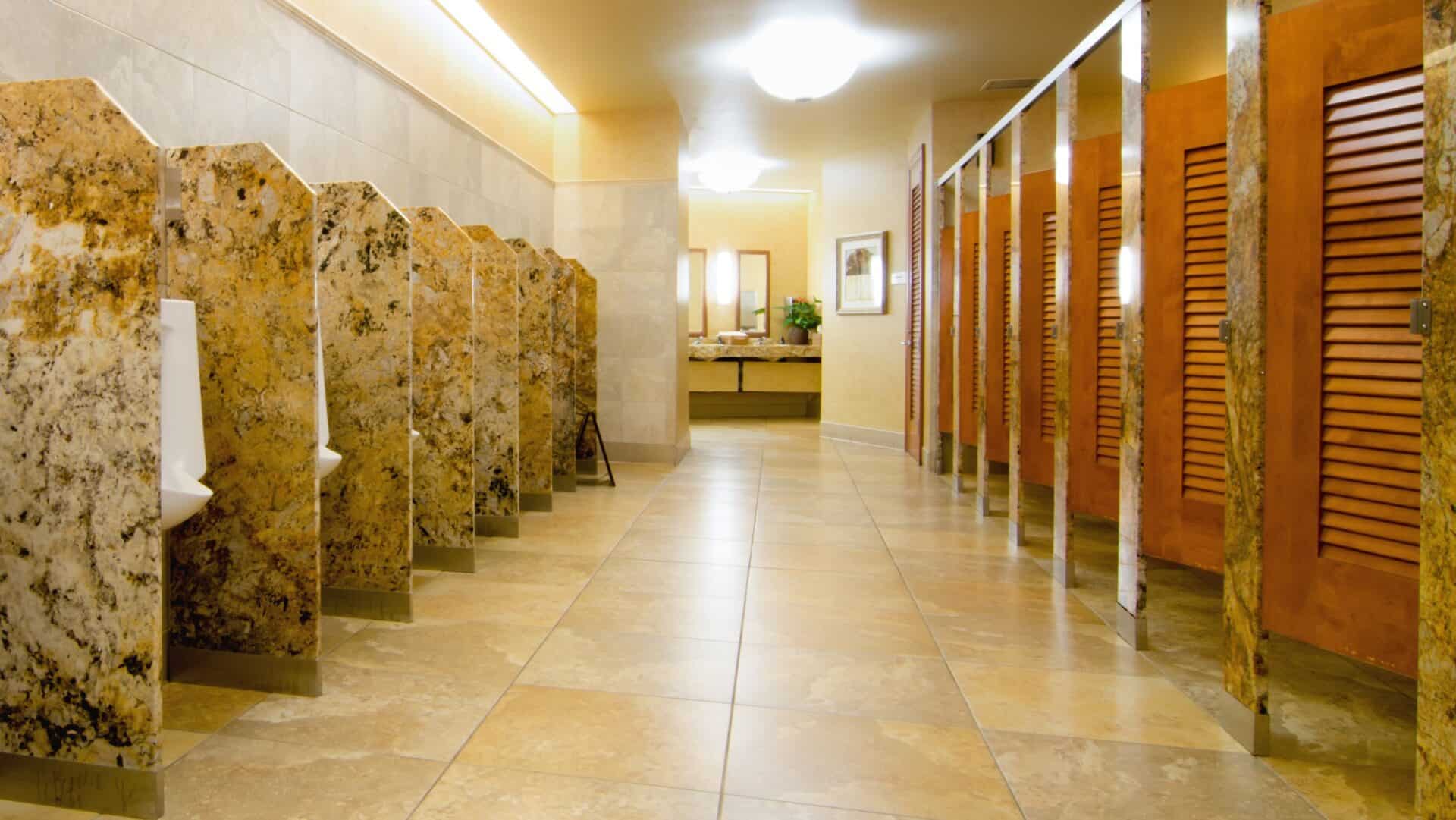 Custom shape stone urinal screens and louvered partition doors in a commercial restroom.